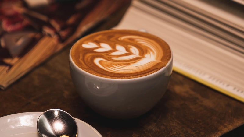 Ground Central cappuccino with leaf latte art on a wooden table next to an open book