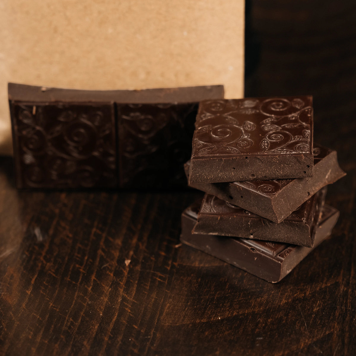 Close-up of stacked embossed Ground Central dark chocolate squares in front of the kraft package