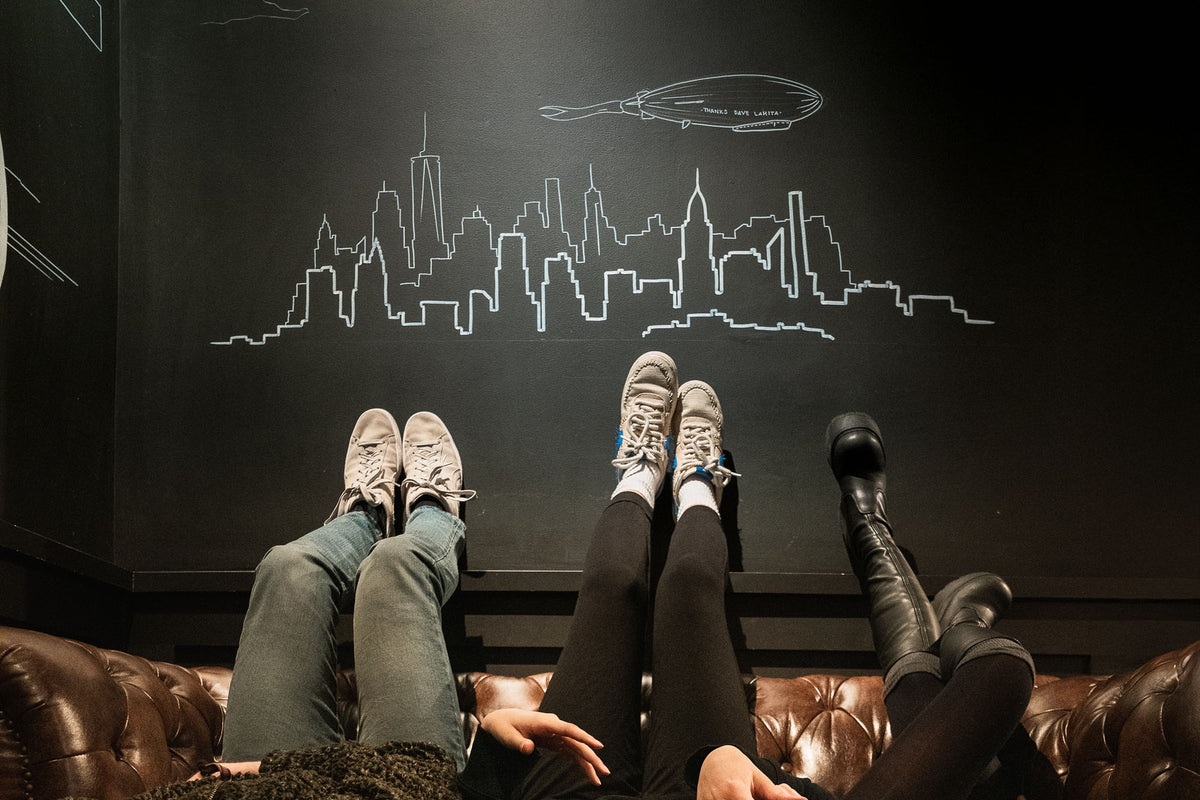 Customers relaxing on a leather sofa below the chalk skyline mural at GC Fashion District